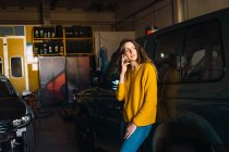 Frau telefoniert mit Smartphone, während sie sich in Garage an Auto lehnt — Stockfoto