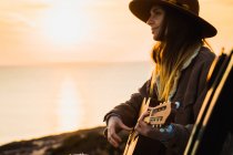 Frau spielt bei Sonnenuntergang am Meer Gitarre — Stockfoto