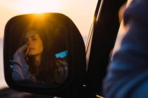 Відображення вдумливої туристичної жінки, що сидить в машині на заході сонця — стокове фото