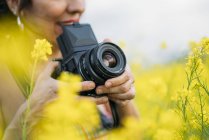 Primo piano della donna con fotocamera retrò scattare foto in natura con fiori gialli — Foto stock