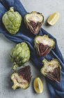 Alcachofras frescas cortadas pela metade com pano azul e pedaços de limão — Fotografia de Stock