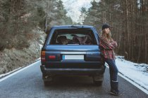 Женщина опирается на автомобиль на дороге в горах — стоковое фото