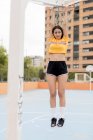 Slim woman in sportswear hanging on basketball hoop outdoors in city — Stock Photo