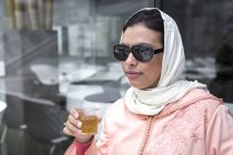 Марокканская женщина с хиджабом и типичным арабским платьем пьет чай в кафе — стоковое фото
