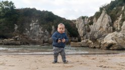 Portrait of toddler boy standing on lake shore with rocks — Stock Photo