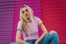 Portrait de jeune femme blonde assise contre un mur multicolore — Photo de stock