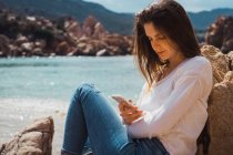 Женщина с помощью смартфона в скалах на берегу моря — стоковое фото
