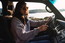 Молодая женщина в солнцезащитных очках за рулем автомобиля на природе — стоковое фото