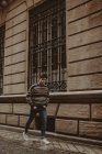 Joven adolescente confiado en suéter caminando por la calle de la ciudad y mirando a la cámara - foto de stock