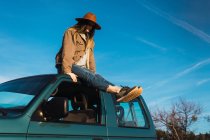 Woman sitting on car roof in nature under blue sky — Stock Photo