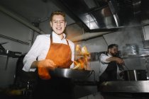 Приготовление фламбе на кухне ресторана с коллегой на заднем плане — стоковое фото