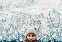 Человек в теплой одежде стоит у белой стены, украшенной голубым орнаментом — стоковое фото
