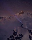 Caminante irreconocible con luz en la cabeza de pie en la montaña cubierta de nieve por la noche - foto de stock