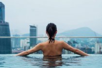 Femme asiatique se détendre dans la piscine avec vue sur la ville sur le fond — Photo de stock