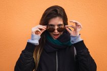 Aufgeregte Frau hebt Brille gegen orangefarbene Wand — Stockfoto