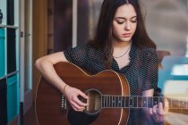 Вдумчивая молодая женщина играет на гитаре — стоковое фото