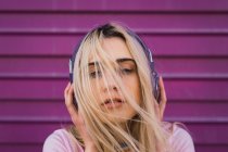 Portrait of young woman with purple headphones in front of pink wall — Stock Photo