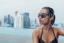 Досить азіатська жінка в сонцезахисних окулярах в душі басейну в місті — стокове фото