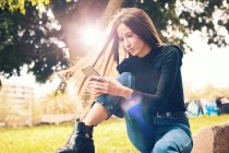Молода жінка сидить на скелі і використовує смартфон у парку — стокове фото