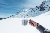 Hand of unrecognizable tourist holding metal cup in mountains in winter — Stock Photo