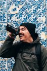 Веселий чоловічий турист стоїть біля стіни з блакитною плиткою і фотографує — стокове фото