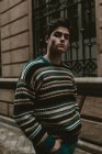 Молодой уверенный в себе подросток в свитере ходит по городской улице и смотрит в камеру — стоковое фото