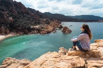 Туристка сидит на скале и смотрит на залив — стоковое фото