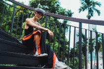 Молодая азиатка в стильной одежде стоит у забора в парке и смотрит в камеру — стоковое фото