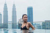 Femme asiatique se détendre dans la piscine avec des gratte-ciel sur fond — Photo de stock