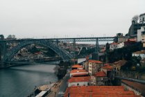 Puente sobre canal y ciudad vieja con techos anaranjados en nublado, Oporto, Portugal - foto de stock
