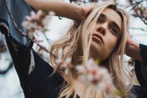 Young blonde woman in flowers standing and holding head — Stock Photo