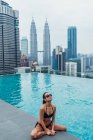 Азиатская расслабленная женщина сидит у бассейна с небоскребами на заднем плане — стоковое фото