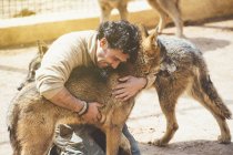 Lächelnder Mann umarmt braune Wölfe im Zoo — Stockfoto