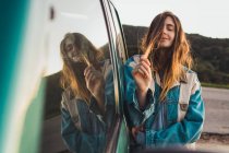 Mujer bastante joven apoyándose en el coche y tocando el cabello en la naturaleza - foto de stock
