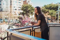 Mujer joven soñadora de pie y fumando en el balcón de la ciudad - foto de stock