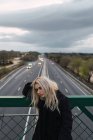 Pensativo loira mulher de pé em cerca na ponte sobre estrada — Fotografia de Stock