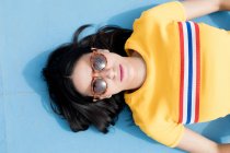 Woman in sportswear and sunglasses lying on blue background — Stock Photo