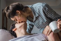 Leidenschaftliches junges Paar mit Tasse küssen auf Couch zu Hause — Stockfoto