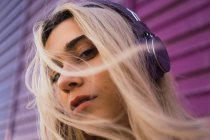 Gros plan de jeune femme blonde avec des écouteurs violets contre le mur violet — Photo de stock