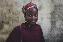 КАМЕРУН - Африка - 5 апреля 2018 года: Красивая африканская женщина в красной традиционной одежде стоит у грубой стены и смотрит в камеру — стоковое фото