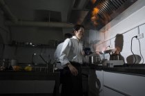 Cozinhar fazendo um flambe na cozinha do restaurante com colega no fundo — Fotografia de Stock