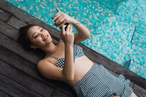 Усміхнена жінка використовує смартфон, розслабляючись у басейні — стокове фото