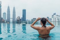 Mujer asiática relajándose en la piscina con vista a la ciudad en el fondo - foto de stock
