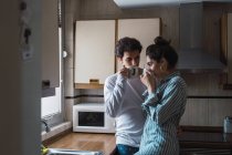 Young couple in pajamas drinking from cups in kitchen — Stock Photo