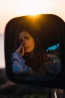 Відображення вдумливої туристичної жінки, що сидить в машині на заході сонця — стокове фото
