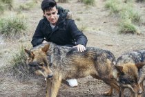 Junger Mann sitzt im Zoo und streichelt Wölfe — Stockfoto