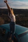 Woman standing on window of car with raised arms in nature — Stock Photo