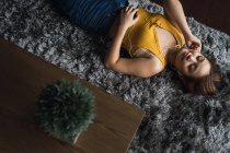 Relaxed woman with earphones lying on carpet — Stock Photo