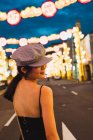 Mujer asiática joven de moda mirando hacia otro lado en la ciudad iluminada por la noche - foto de stock