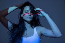 Giovane donna attraente con linea rossa sul viso e sul corpo guardando la fotocamera su sfondo scuro — Foto stock